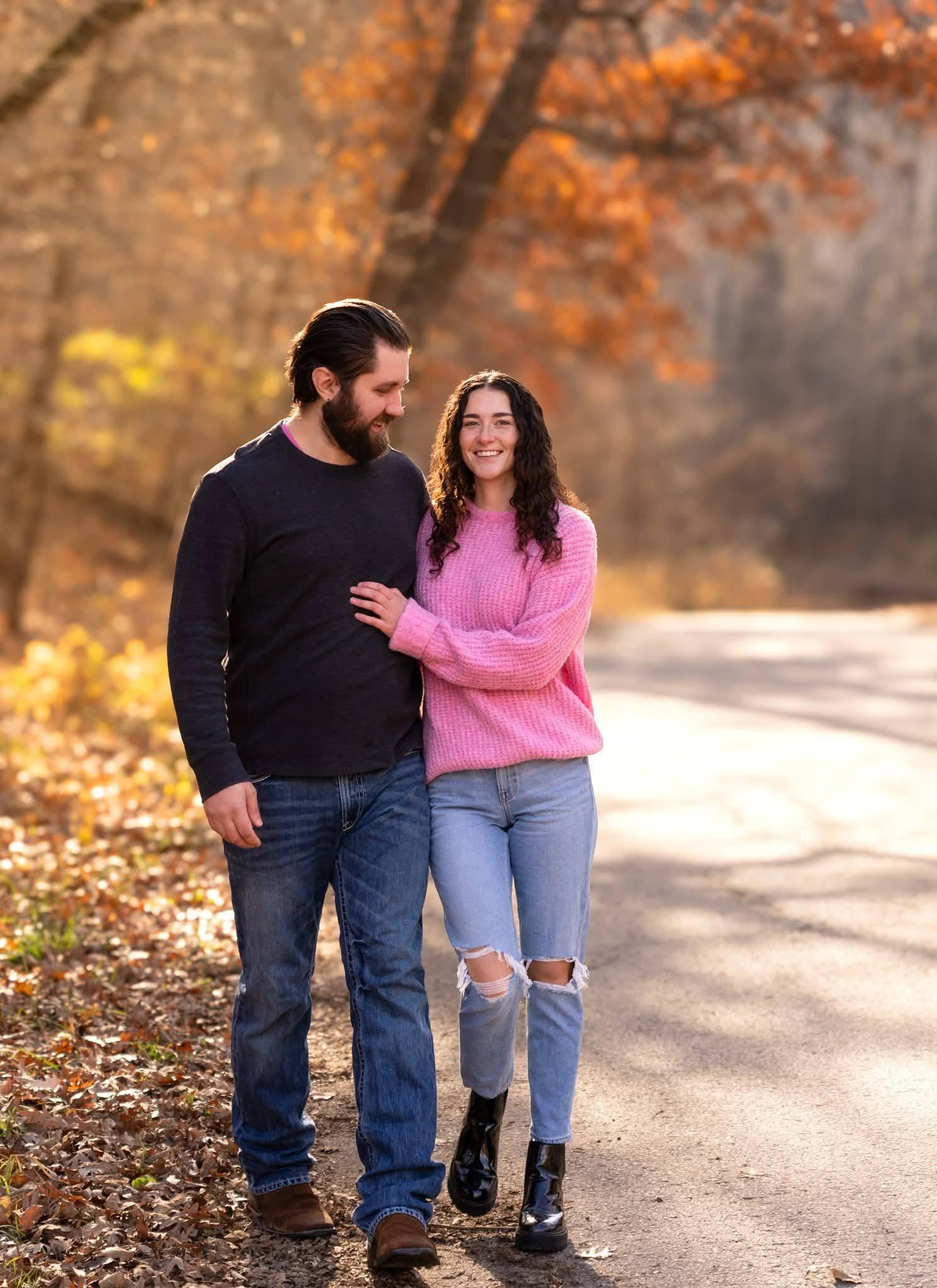 A couple walking a sunlit path lined with autumn trees