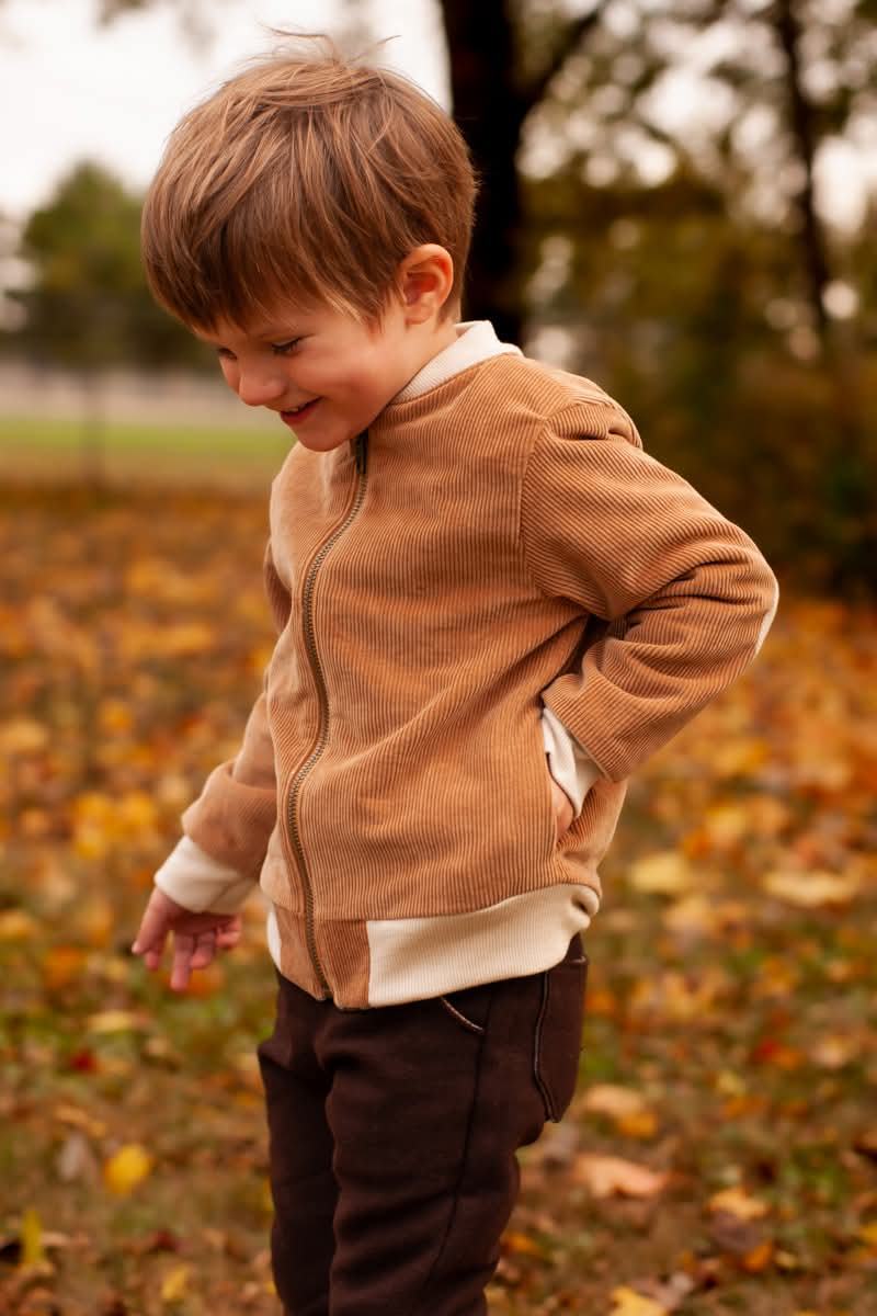 A boy in a tan jumper looking down at fallen leaves