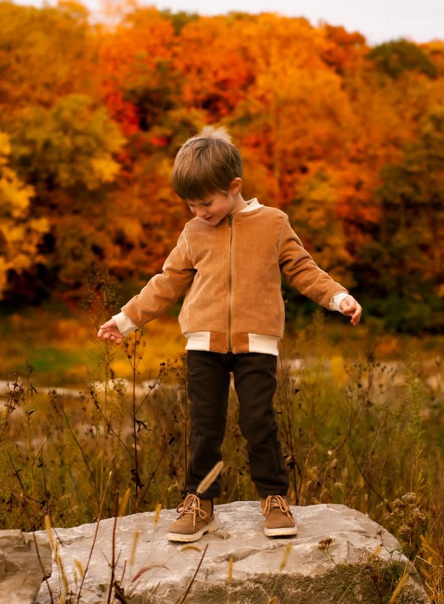 A young boy standing on a rock in front of bright red autumn foliage