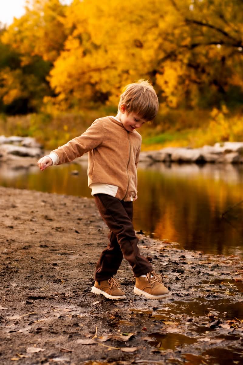 A boy skipping stones at the edge of a creek in autumn