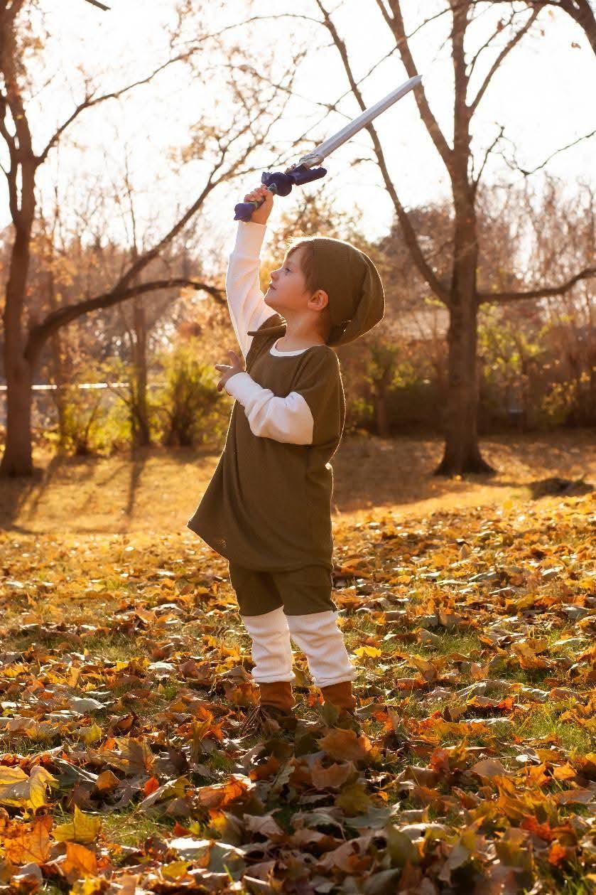 A small boy in costume raising a toy sword above his head