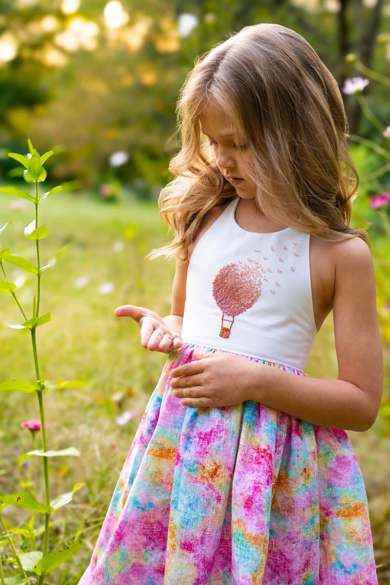 A girl in a floral dress reaching towards wildflowers
