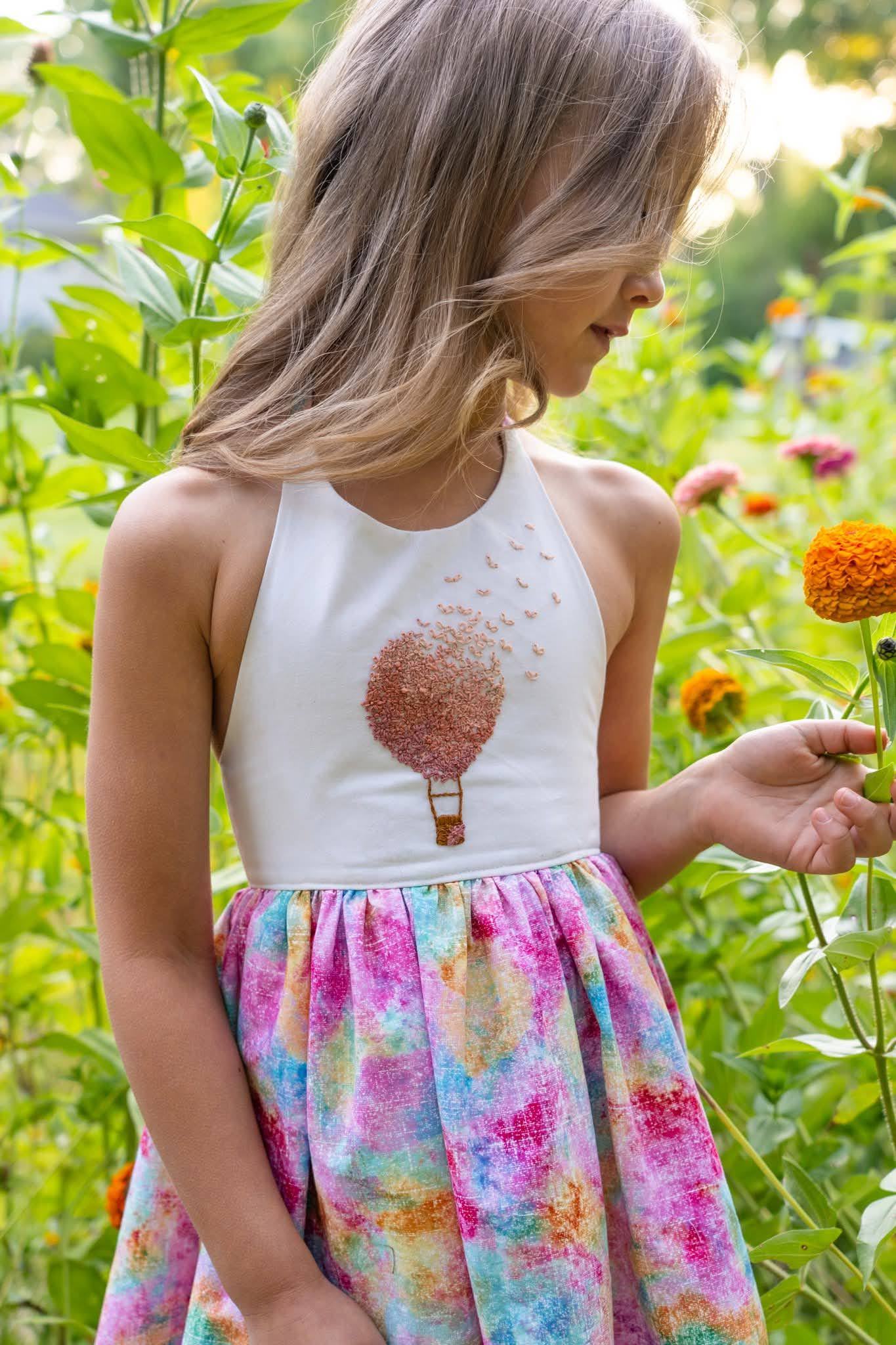 A girl holding a single orange flower up to look at it