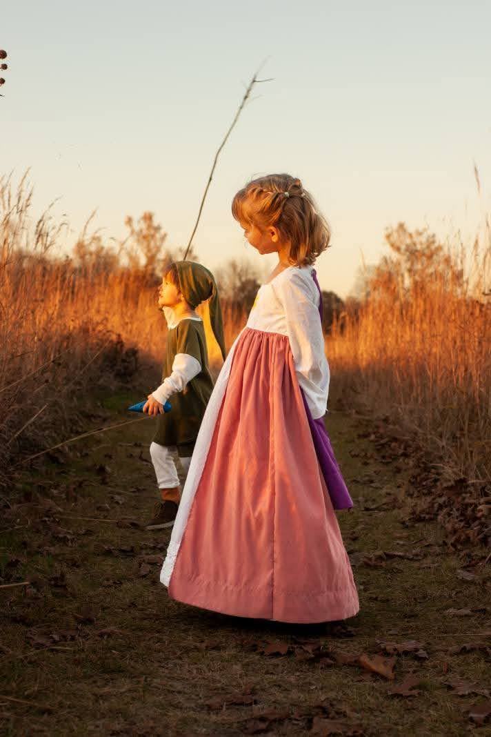 Two children in dress-up costumes walking through a winter field