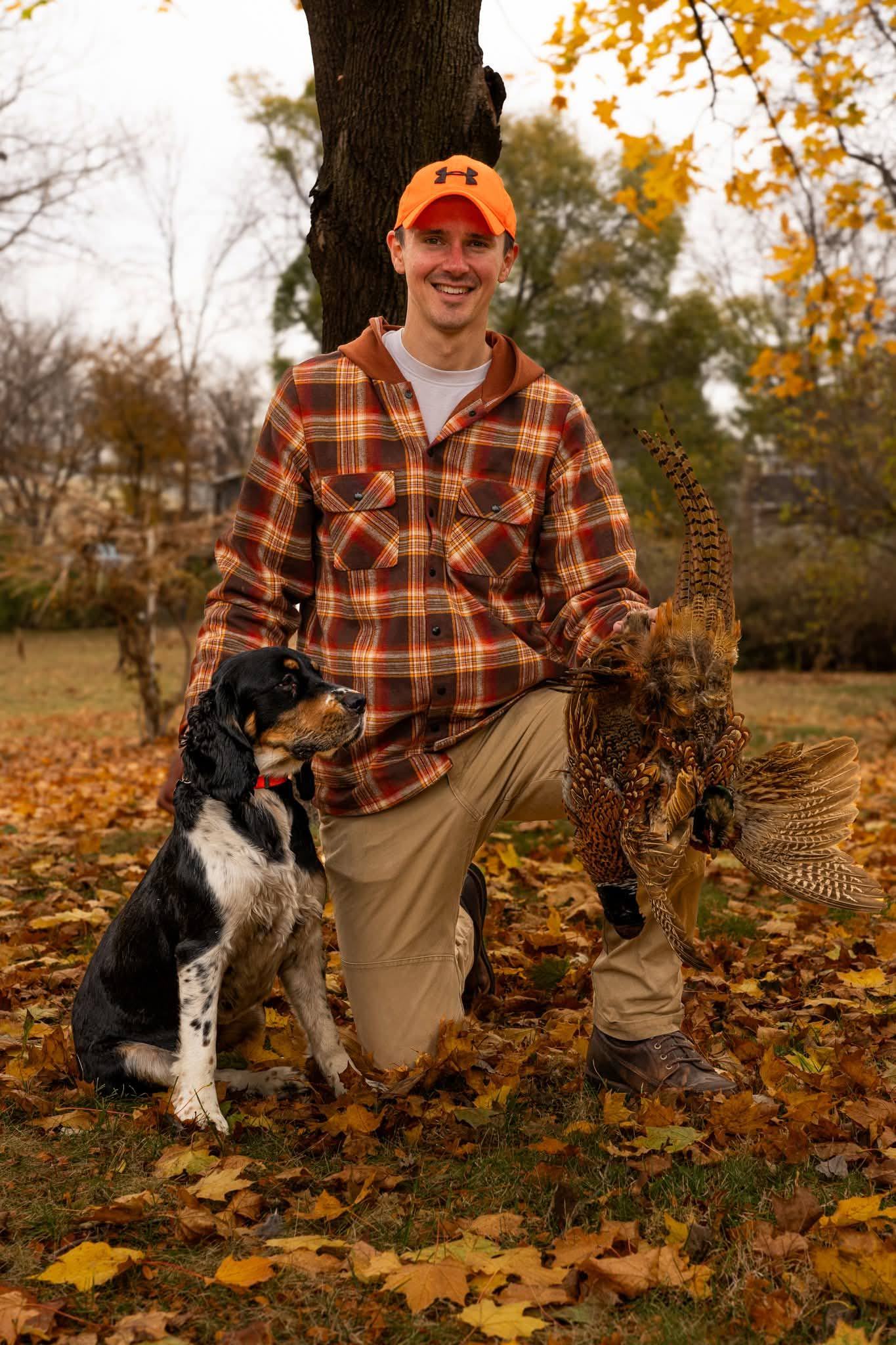 A man kneeling in autumn leaves beside his spaniel