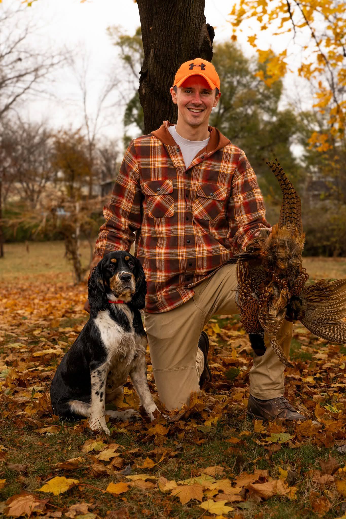 A man in a plaid jacket kneeling with his dog in a field
