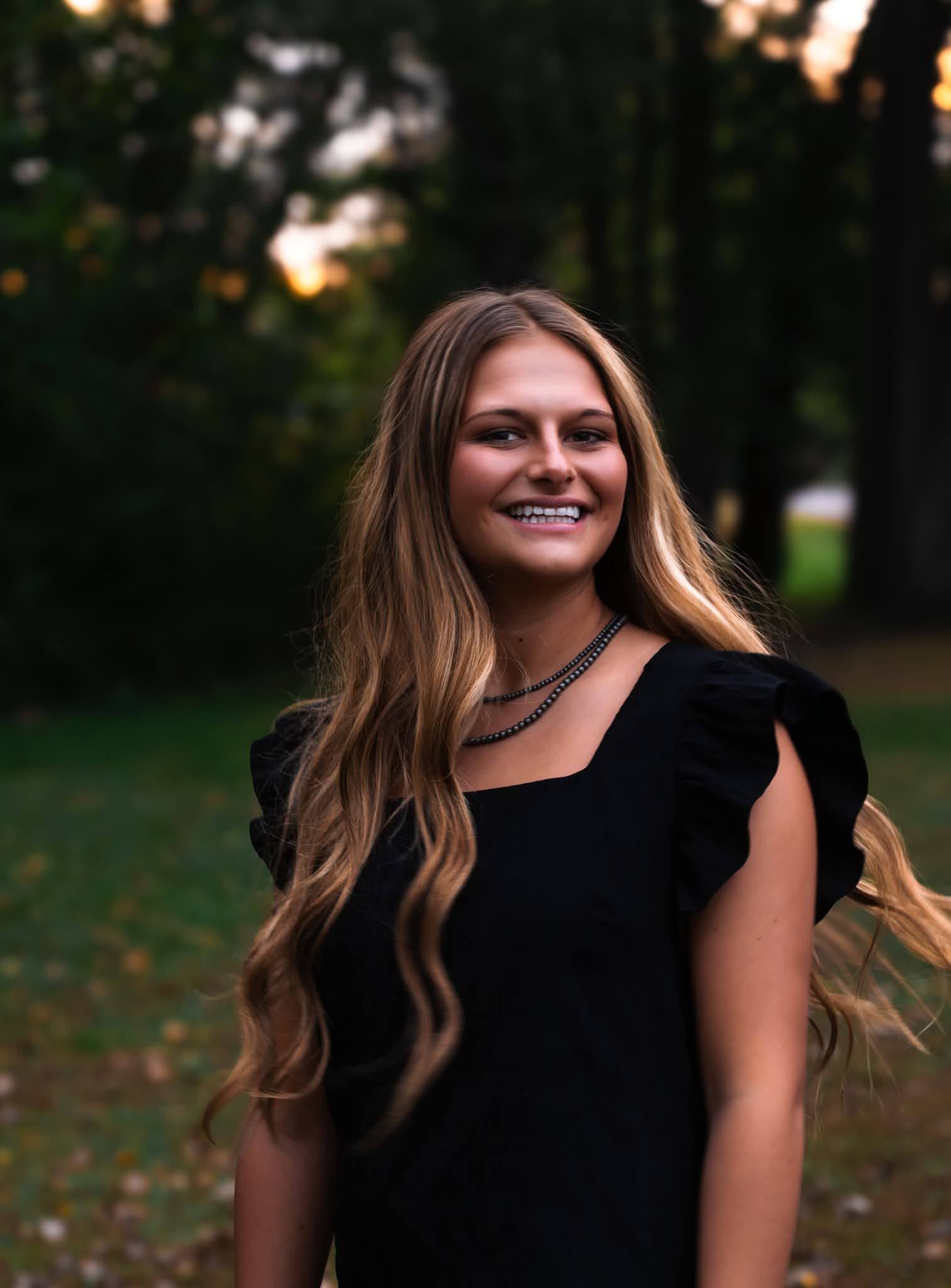 A high school senior in a black dress smiling in evening light