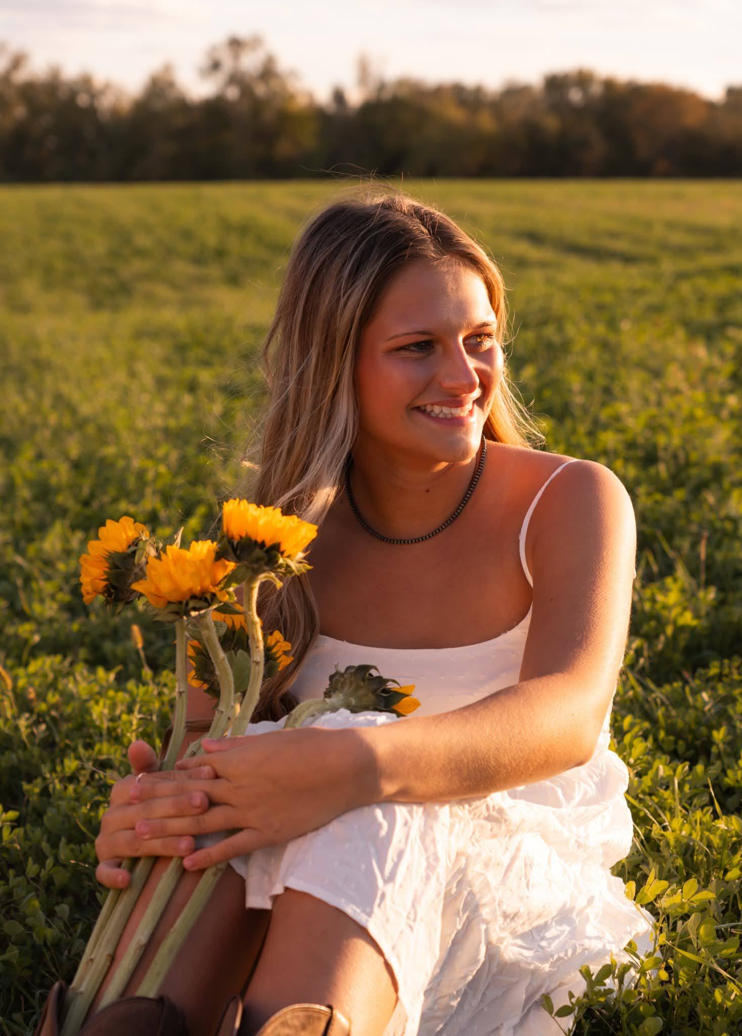 A senior in a white dress holding a bunch of sunflowers in a field